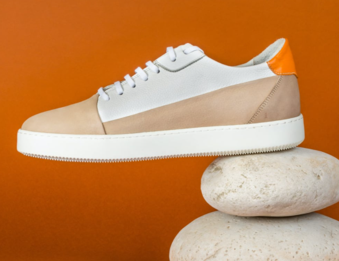 Sideview of tan, brown, and orange sneaker with flat tread placed onto of two flat rocks