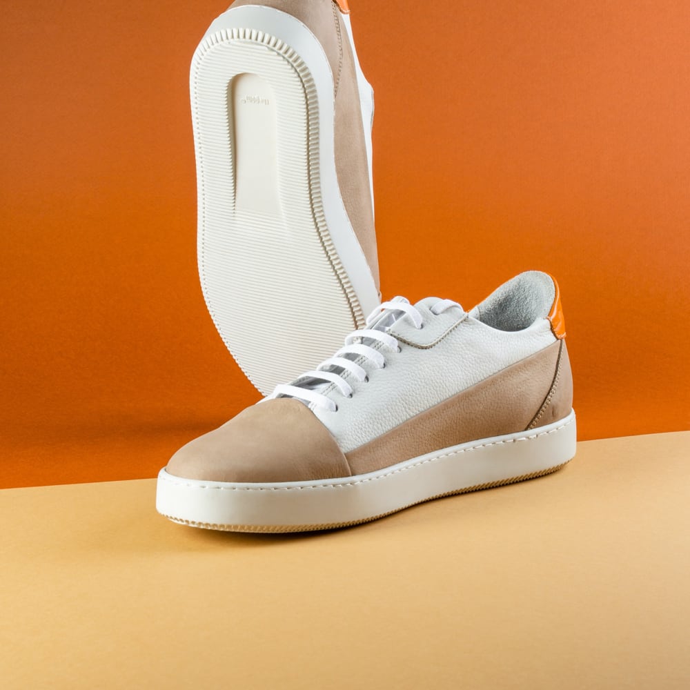 A pair of tan and white sneakers with white shoelaces and flat tread